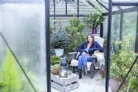 Woman sitting on chair with hot drink inside decorated greenhouse