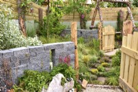 Opened wooden gates leading to grassy-gated dog area in the woodland inspired garden surrounded by a wooden planks fence with a decorative Connemara walling system. Planted with Astilbe, fungi, grasses. June
Designer: Mary Anne Farenden. Bord Bia Bloom, Super Garden, Dublin, Ireland.

