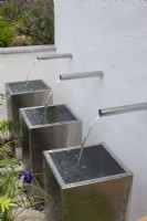 Three chrome water spouts cascading into metal containers in the 'Sociability' garden at BBC Gardener's World Live 2015, June