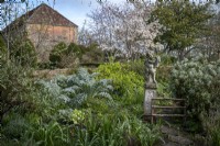 A statue is a focal point in the spring cottage garden at East Lambrook Manor, with an Amelanchier lamarckii behind