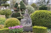 Statue of Britannia with latin inscription and terracotta pots with tulips. Topiary of Yew and box behind. April. Spring. 