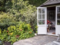 Small summerhouse and patio next to a mixed border featuring Smyrnium perfoliatum, Erysimum, Rubus deliciosus, Euonymus fortunei, Polygontatum and Tulipa 'Brown Sugar'
