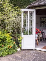 Summerhouse doorway next to a mixed border featuring Smyrnium perfoliatum, Rubus deliciosus, Euonymus fortunei, Myosotis, Polygontatum and Tulipa 'Brown Sugar'