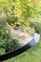 View of the edge of the garden showing circular rill and shade planting of Acer, ferns, thalictrum and aquilegia. The Macmillan Legacy Garden at RHS Malvern Spring Festival 2024. Designed by TJ Kennedy and Kerianne Fitzpatrick