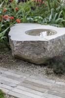 Stone bird bath with planting behind set into Yorkstone paving and recycled glass sand  - 'It Doesn't Have to Cost the Earth' - designer Michael Lote - RHS Malvern Spring Festival 2024