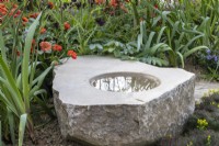 Stone bird bath with planting including Geum 'Scarlet Tempest'  - 'It Doesn't Have to Cost the Earth' - designer Michael Lote - RHS Malvern Spring Festival 2024