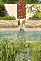 Wall with steel panel with feature a water cascade, flowing into a rill that runs to the main pool and stones raised beds with exotic plants in Mediterranean garden. June
Designer: Alan Rudden