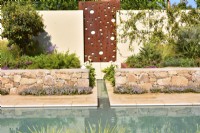 Wall with steel panel with feature a water cascade, flowing into a rill that runs to the main pool and stones raised beds with exotic plants in Mediterranean garden. June
Designer: Alan Rudden


