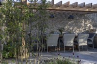 Outdoor dining area on a Yorkstone terrace with Cotswold stone wall and wooden pergola on The Cotswold Garden - designer Mark Draper Graduate Gardeners - RHS Malvern Spring Festival 2024