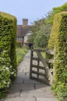 View of an open wooden gate entrance along a stone path in an informl country cottage garden in early Summer - May