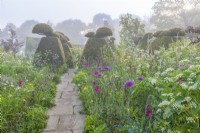 View along a stone path of borders of mixed annuals bulbs and perennials flowering in an informal country cottage garden in early Summer - May