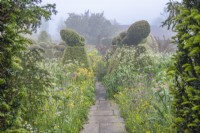 View along a stone path of borders of mixed annuals bulbs and perennials flowering in an informal country cottage garden in early Summer - May