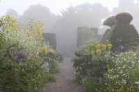 View of gravel path between borders in an informal country cottage garden in early Summer - May