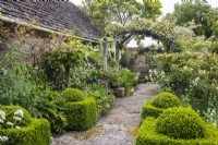 Clipped box topiary edges a path leading under a pergola at Oxleaze Farm, Gloucestershire.